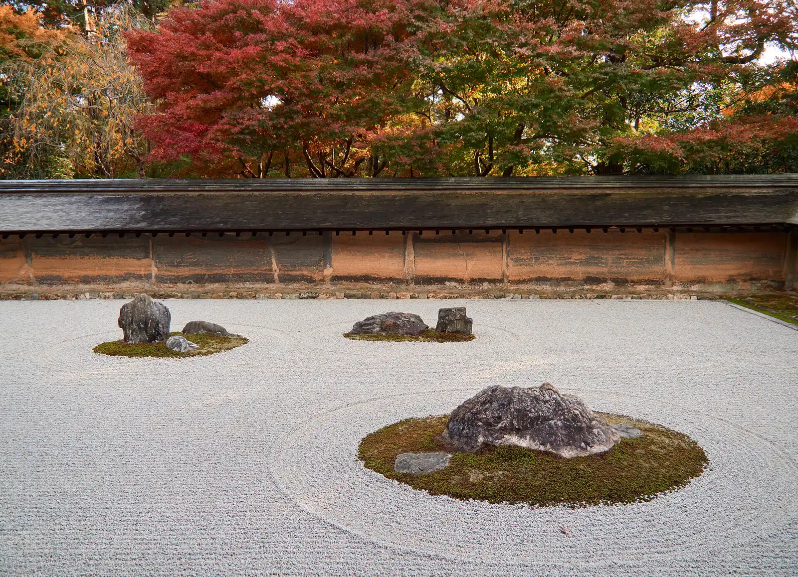 Japanese garden at Ryōan-ji: raked white gravel circling three moss-ringed rock groups before an old clay wall